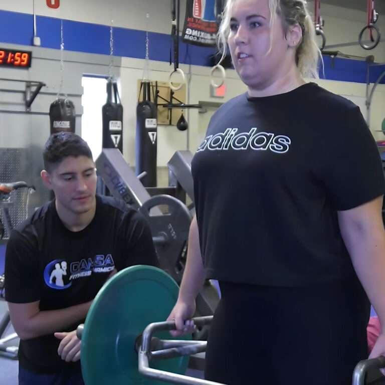 Woman lifting weights with a hex trap bar alongside personal trainer
