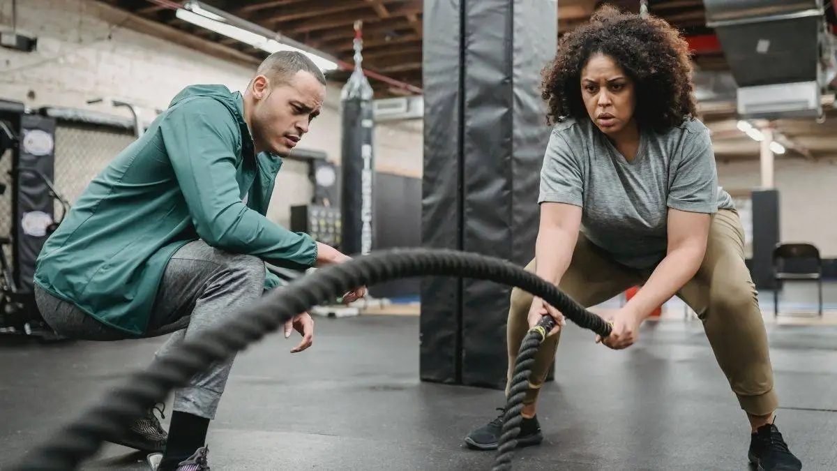 Fitness trainer guiding woman through battle rope exercise